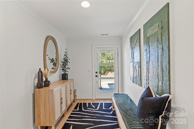 doorway featuring ornamental molding, visible vents, and light wood-style flooring