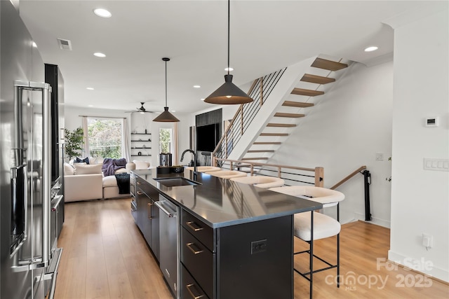 kitchen with light wood finished floors, visible vents, a breakfast bar, stainless steel appliances, and a sink