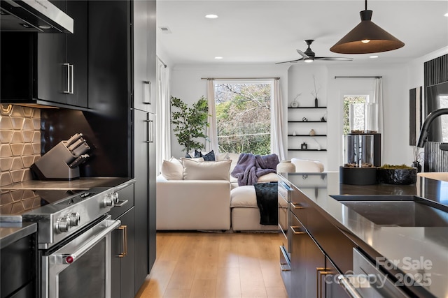 kitchen featuring under cabinet range hood, a sink, appliances with stainless steel finishes, backsplash, and light wood finished floors