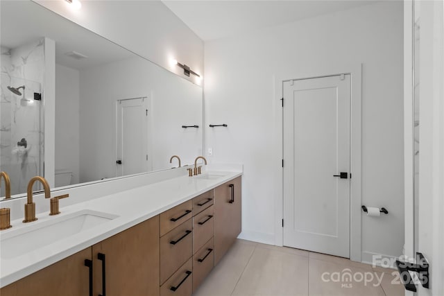 bathroom with toilet, double vanity, a marble finish shower, and a sink