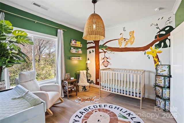 bedroom featuring a crib, baseboards, visible vents, wood finished floors, and crown molding