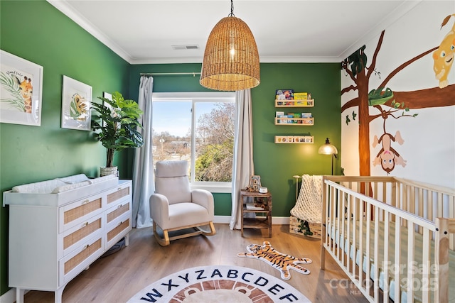 bedroom with ornamental molding, visible vents, a crib, and wood finished floors