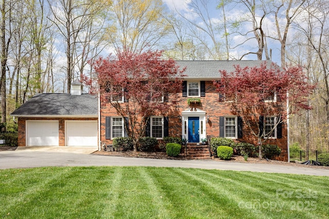 colonial house featuring brick siding, driveway, a front lawn, and an attached garage