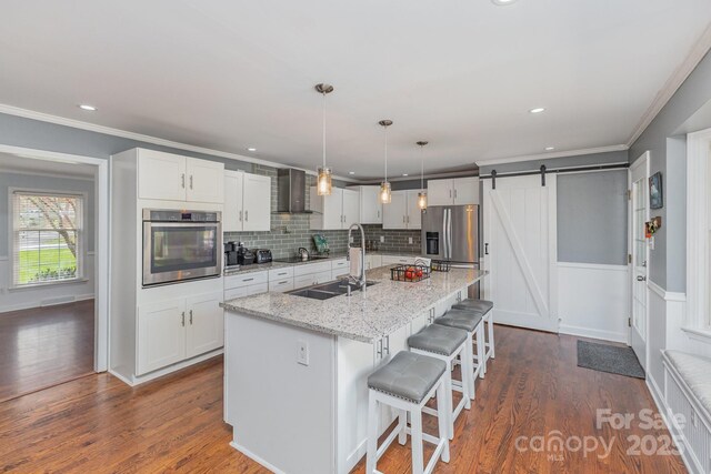 kitchen featuring dark wood-style flooring, wall chimney exhaust hood, appliances with stainless steel finishes, white cabinetry, and a sink