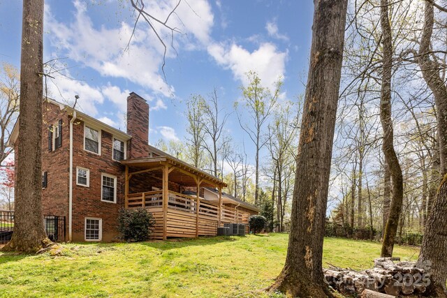 rear view of property featuring a chimney, central air condition unit, brick siding, and a yard