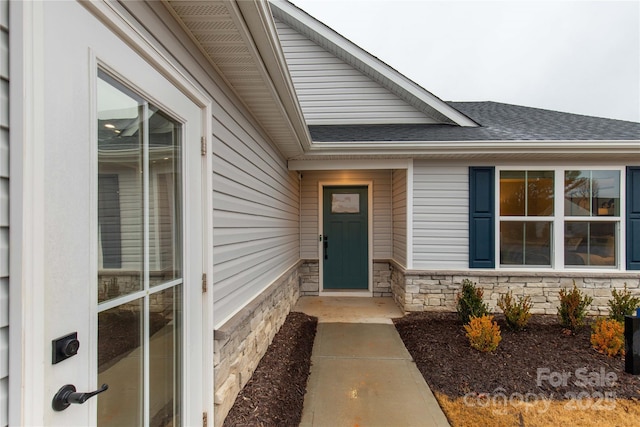 doorway to property with a shingled roof and stone siding