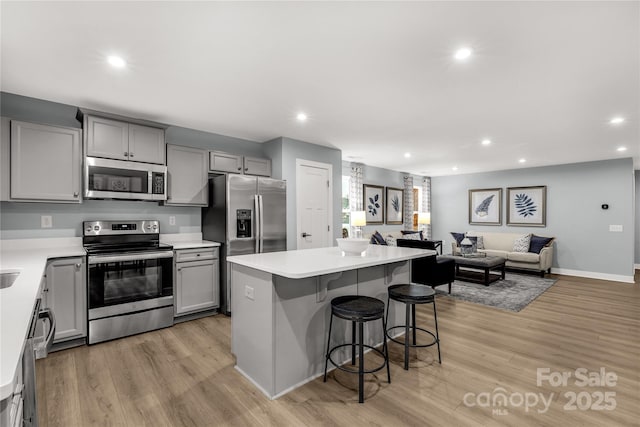 kitchen with a kitchen breakfast bar, open floor plan, gray cabinets, stainless steel appliances, and light wood-style floors