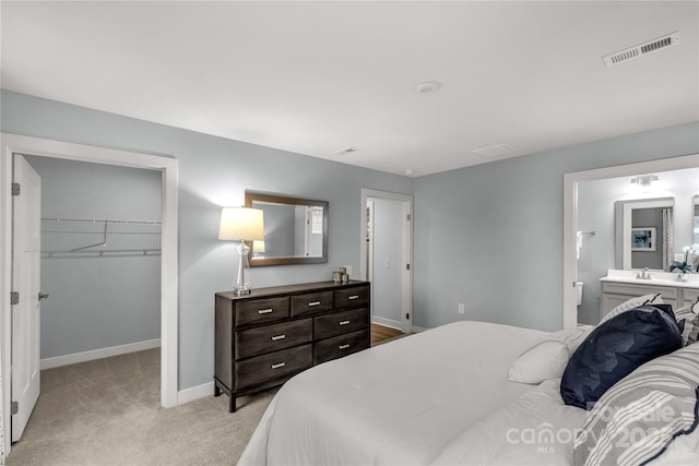 bedroom featuring baseboards, visible vents, light colored carpet, a walk in closet, and a closet