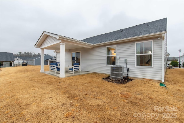 back of house featuring roof with shingles, a patio area, a lawn, and central AC unit