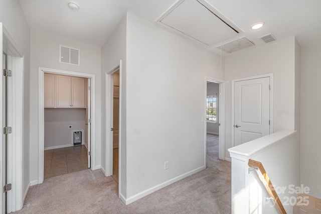 corridor with light carpet, visible vents, attic access, and baseboards