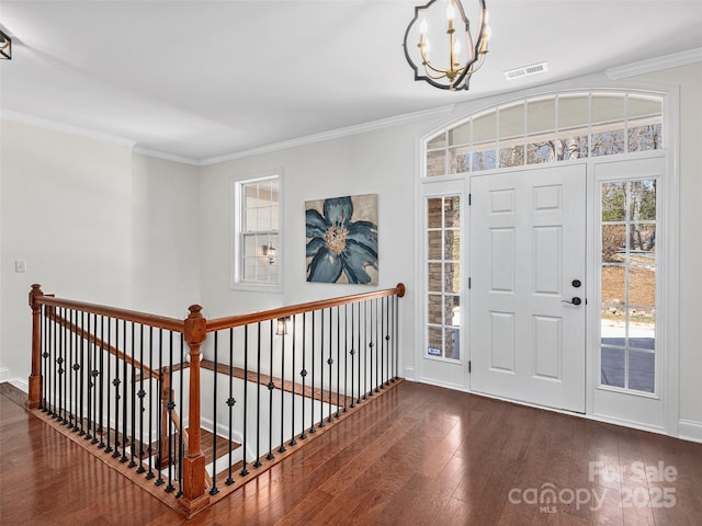 foyer with baseboards, visible vents, ornamental molding, hardwood / wood-style floors, and an inviting chandelier