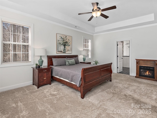 carpeted bedroom with baseboards, connected bathroom, a glass covered fireplace, ornamental molding, and a tray ceiling