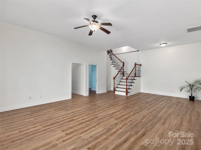 unfurnished room with wood finished floors, visible vents, baseboards, and stairs