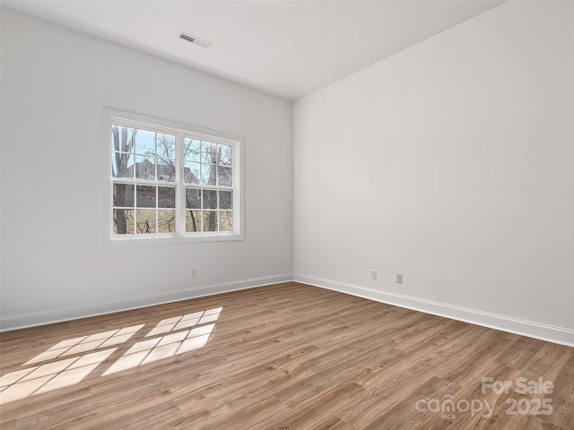 empty room featuring baseboards, visible vents, and wood finished floors