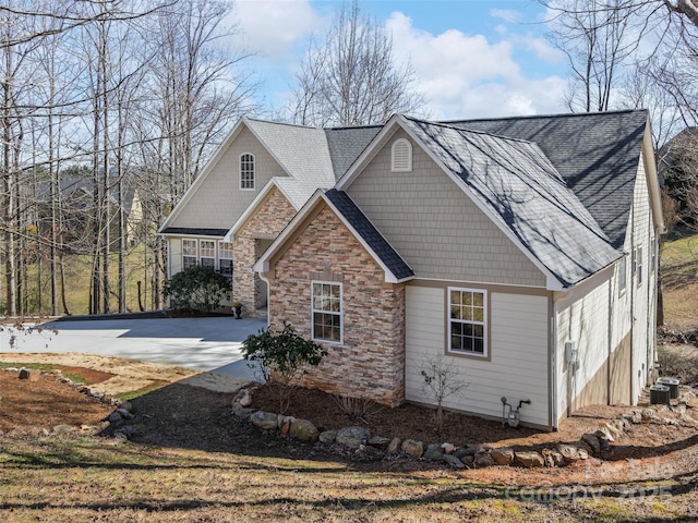 view of front of home with stone siding, a shingled roof, central AC unit, and concrete driveway