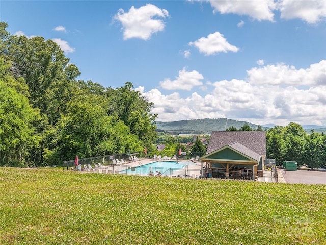 community pool featuring a mountain view, a patio area, fence, and a lawn