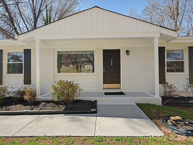 view of exterior entry with a porch and brick siding