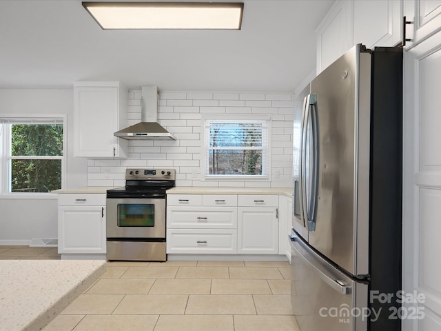 kitchen featuring decorative backsplash, appliances with stainless steel finishes, light countertops, wall chimney range hood, and light tile patterned flooring