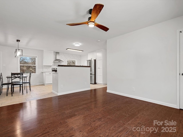 unfurnished living room featuring ceiling fan, light wood-style flooring, and baseboards