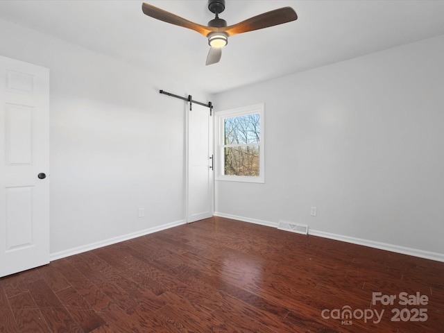 empty room featuring visible vents, a barn door, a ceiling fan, wood finished floors, and baseboards