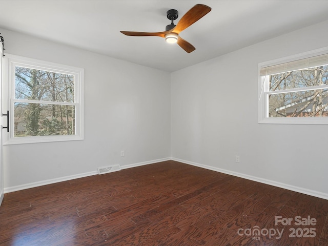 unfurnished room with dark wood-style flooring, visible vents, and baseboards