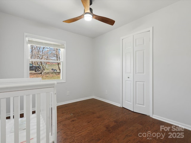 unfurnished bedroom featuring wood finished floors, a ceiling fan, baseboards, a closet, and a nursery area