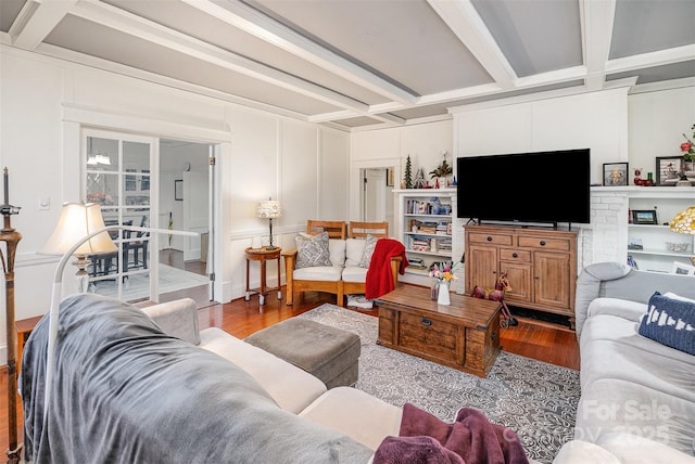 living room featuring beam ceiling, coffered ceiling, a decorative wall, and wood finished floors