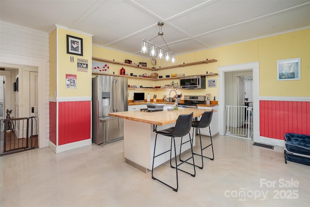 kitchen with a kitchen island, a kitchen breakfast bar, stainless steel appliances, open shelves, and wooden counters