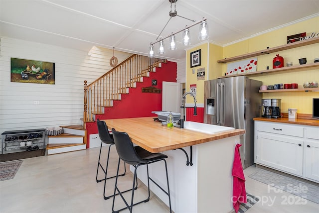 kitchen with finished concrete flooring, butcher block counters, a kitchen bar, and white cabinetry