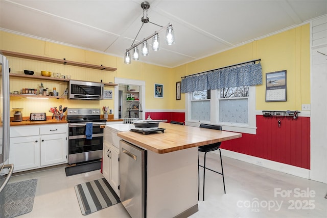 kitchen with a breakfast bar, wood counters, white cabinetry, appliances with stainless steel finishes, and pendant lighting