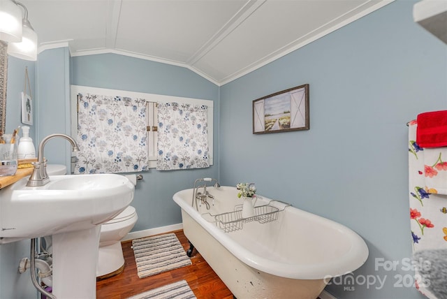 bathroom with wood finished floors, baseboards, vaulted ceiling, ornamental molding, and a soaking tub