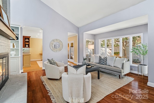 living room with high vaulted ceiling, hardwood / wood-style floors, a glass covered fireplace, and baseboards