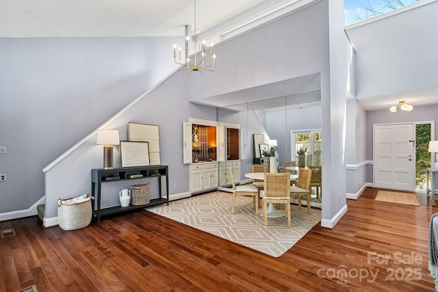 dining room with a high ceiling, wood finished floors, a healthy amount of sunlight, baseboards, and an inviting chandelier