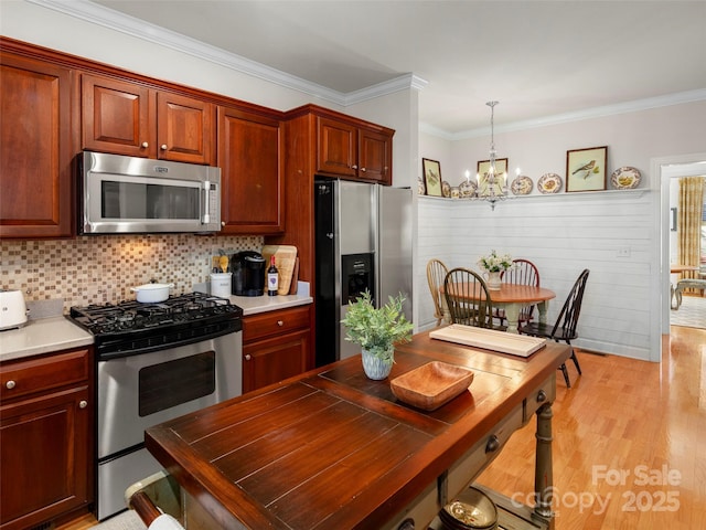 kitchen featuring tasteful backsplash, light wood-style flooring, ornamental molding, stainless steel appliances, and a chandelier