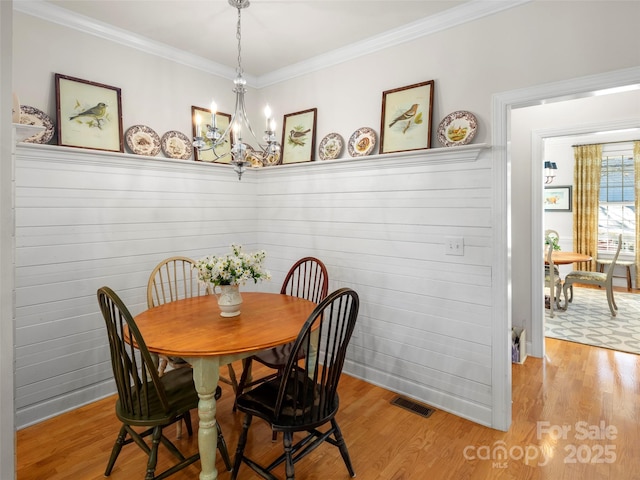 dining area with ornamental molding, light wood finished floors, visible vents, and an inviting chandelier