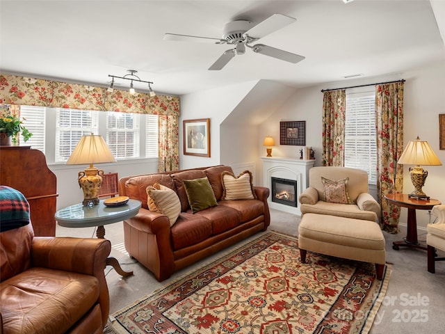 living area with carpet floors, visible vents, a ceiling fan, and a glass covered fireplace