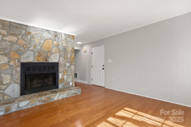 unfurnished living room with ornamental molding, visible vents, a fireplace, and wood finished floors