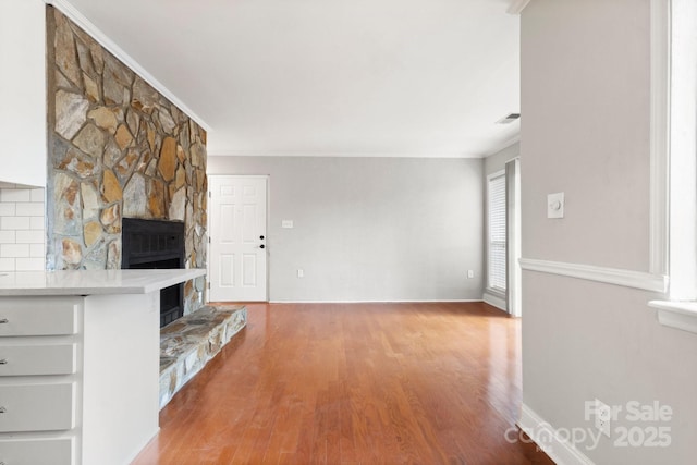 unfurnished living room with a fireplace, wood finished floors, visible vents, baseboards, and ornamental molding