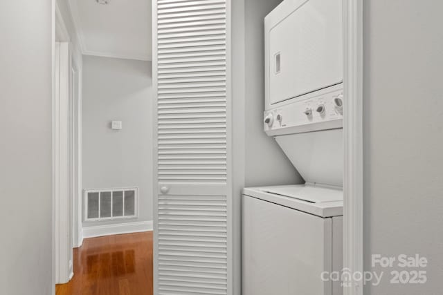 laundry room featuring laundry area, baseboards, visible vents, wood finished floors, and stacked washing maching and dryer