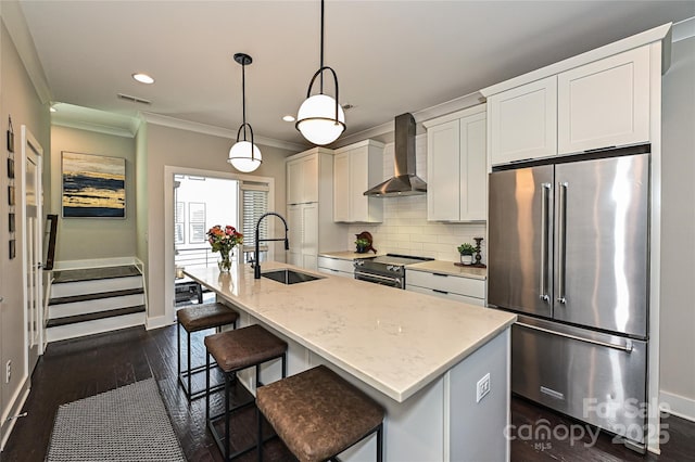 kitchen with stainless steel appliances, a sink, backsplash, wall chimney exhaust hood, and a center island with sink