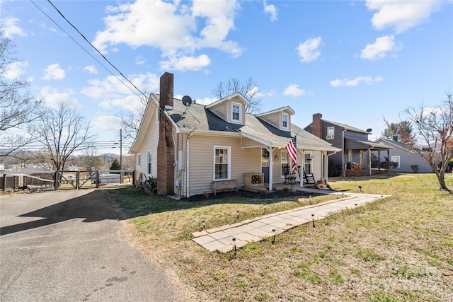 view of front of property featuring a chimney, aphalt driveway, roof with shingles, a gate, and a front lawn