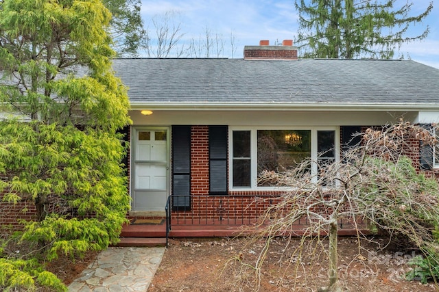 property entrance featuring brick siding, a chimney, and a shingled roof