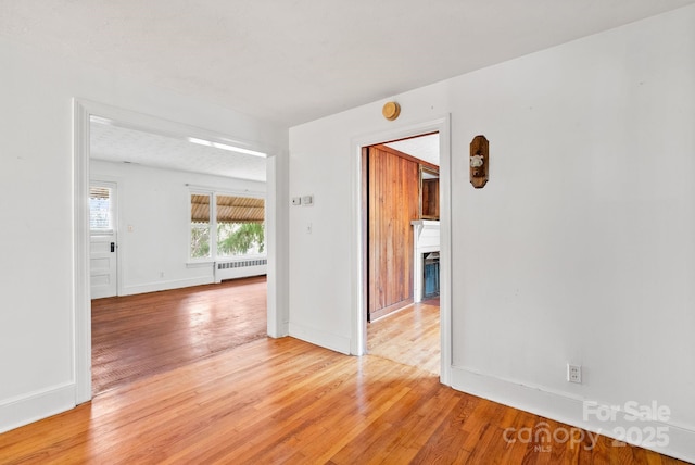 unfurnished room with light wood finished floors, radiator, a fireplace, and baseboards