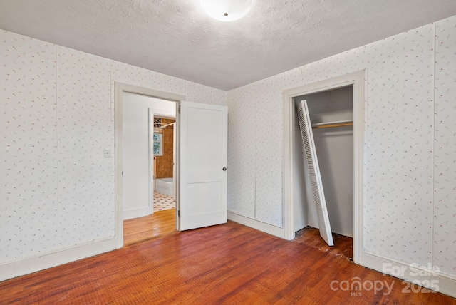 unfurnished bedroom featuring wood finished floors, baseboards, wallpapered walls, a closet, and a textured ceiling