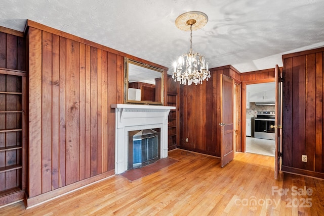 unfurnished living room with a glass covered fireplace, light wood-style flooring, an inviting chandelier, and wood walls