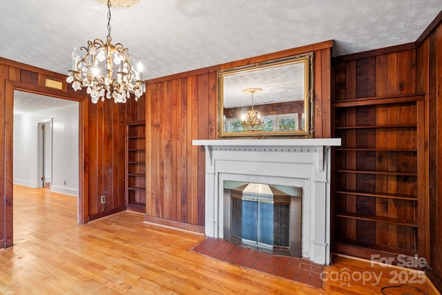 unfurnished living room with built in shelves, a textured ceiling, an inviting chandelier, and wood walls