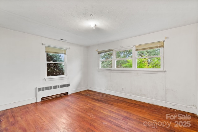 unfurnished room with visible vents, a healthy amount of sunlight, wood finished floors, and radiator heating unit