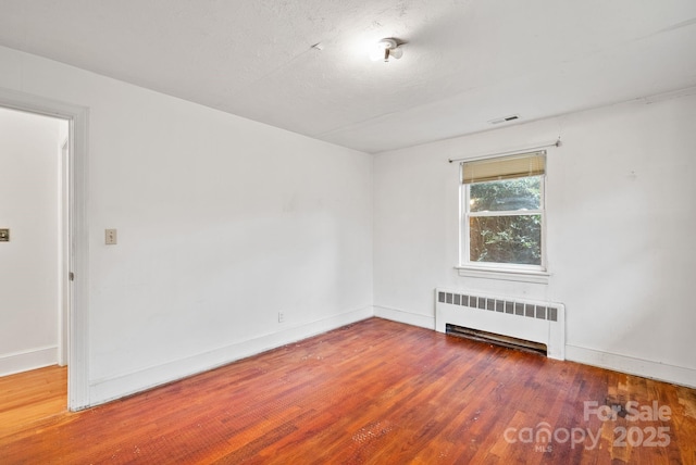 unfurnished room with radiator heating unit, wood finished floors, visible vents, and baseboards