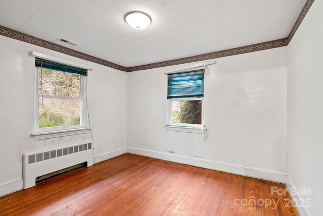 spare room featuring a wealth of natural light, radiator heating unit, baseboards, and hardwood / wood-style flooring