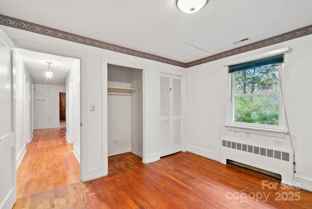 unfurnished bedroom with visible vents, multiple closets, light wood-style floors, radiator, and baseboards